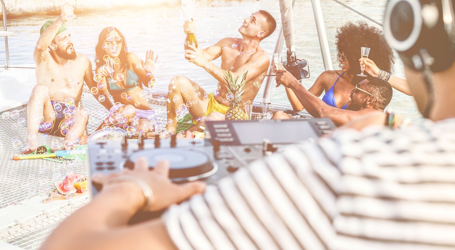 Happy friends drinking champagne in summer boat party - Young millennials people having fun drinking together with dj mixing music - Youth lifestyle and vacation concept - Focus on center man